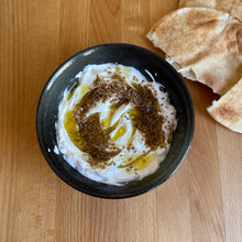 Black bowl of labneh drizzled with extra virgin olive oil and seasoned with dukkah