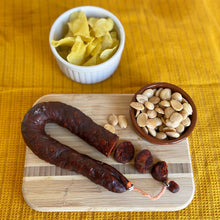 Sliced Spanish chorizo on cutting board with marcona almonds and potato chips